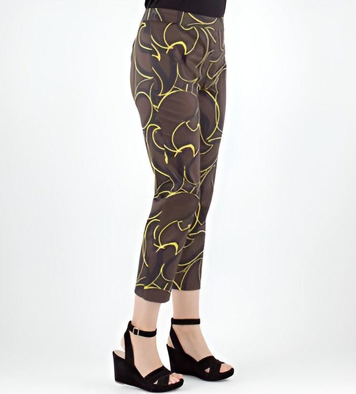 A person wearing brown cropped pants with a yellow abstract line pattern, paired with black wedge sandals, shown against a light gray studio background.