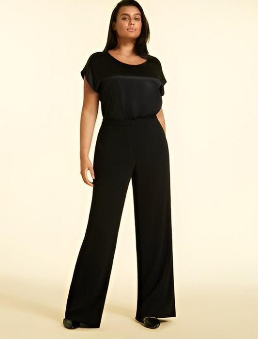 A woman modeling a black jumpsuit with a scoop neckline, short flutter sleeves, and wide-leg pants against a solid cream background.