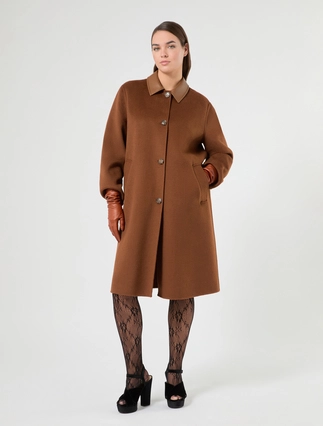 A woman modeling a brown wool-blend coat with a collar, front buttons, and patch pockets, paired with black lace tights and black platform heels, against a light gray studio background.