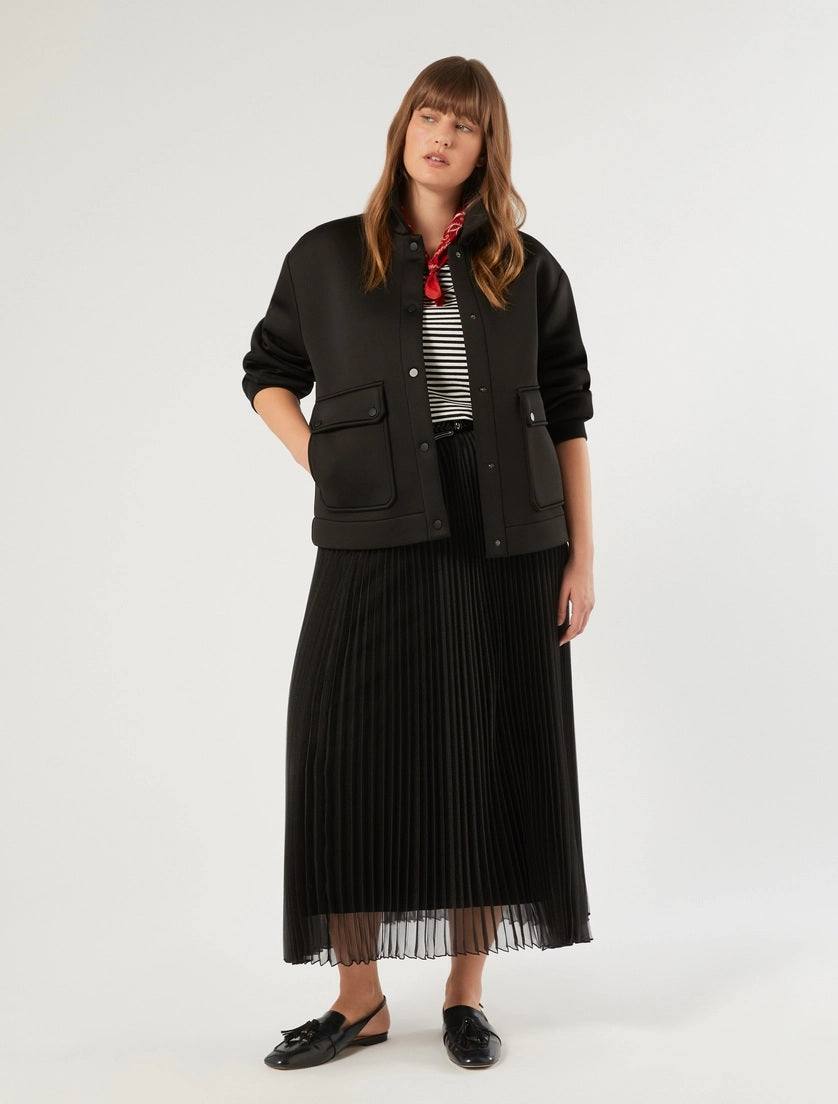 Woman wearing black flared pleated organza skirt with elastic waistband and black jacket