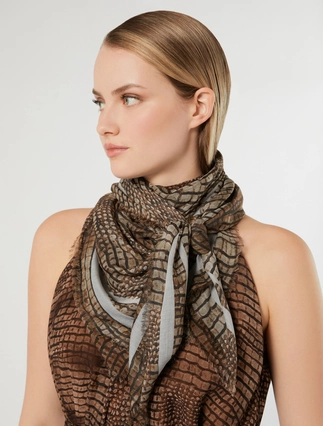 A woman wearing a brown and gray patterned scarf with a textured, reptile-like design, styled around her neck against a light gray studio background.